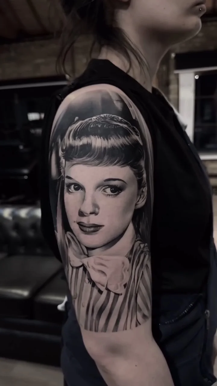 a Judy Garland portrait with a ribbon at the collar, black and grey realism tattoo by Victor Armero, Plymouth