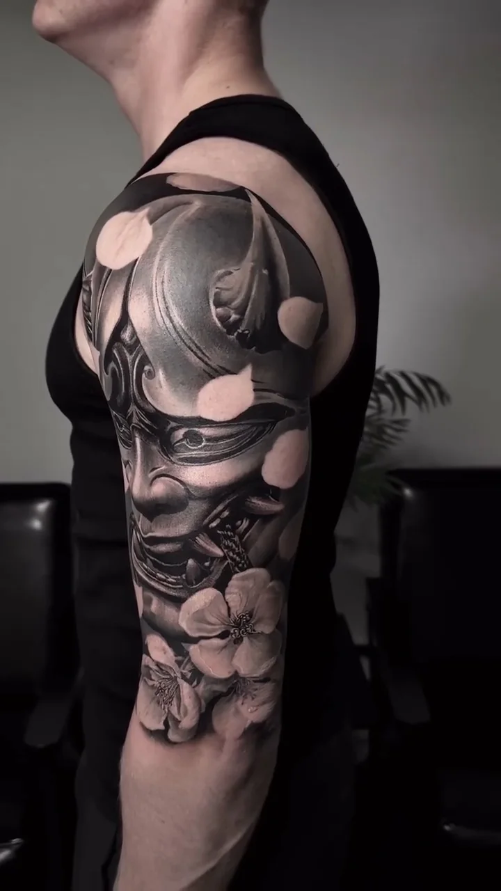 a horned demon mask among cherry blossom, wrapping the sleeve, black and grey realism tattoo by Victor Armero, Plymouth